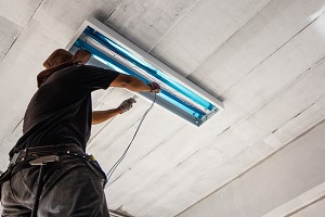 Technician is installing fluorescent bulbs on ceiling of building