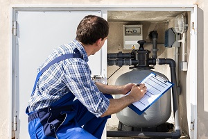 Worker Holding Clipboard Inspecting Water Pump And Pipes | plumbing for commercial spaces